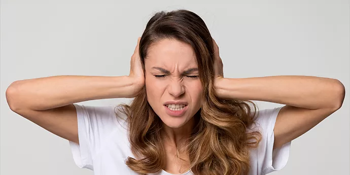 Image qui montre une femme qui se bouche les oreilles à cause des nuisances sonores d'une pompe à chaleur